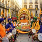 Celebración colorida del Vaisakhi en las calles de Barcelona, con hombres sijs con turbantes naranjas y azules, banderas Nishan Sahib y el logo de ECO NOTICIA.
