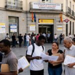 Personas haciendo cola frente a una Oficina de Extranjería en España con documentos para el proceso de regularización de inmigrantes.