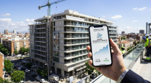 Una mano sosteniendo un teléfono inteligente con un gráfico de crecimiento financiero frente a un edificio residencial en construcción en Madrid.